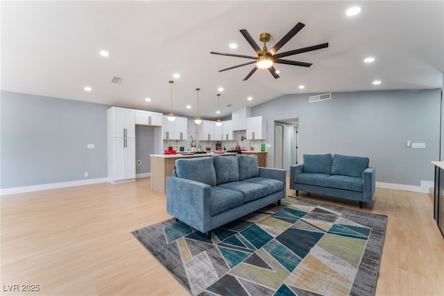 living room with a ceiling fan, vaulted ceiling, light wood finished floors, baseboards, and recessed lighting