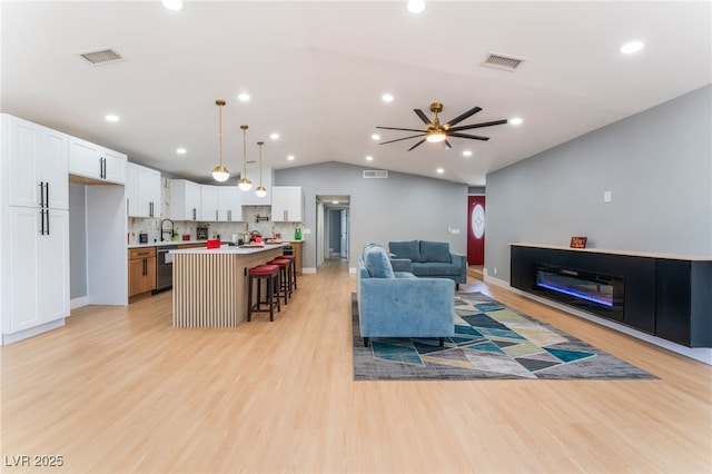 living room with vaulted ceiling, a ceiling fan, light wood-type flooring, recessed lighting, and a glass covered fireplace