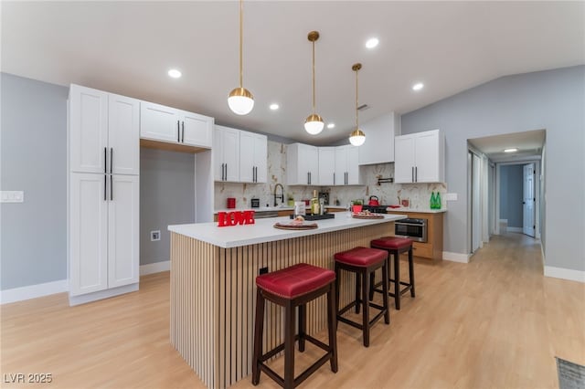 kitchen featuring light wood-style floors, light countertops, tasteful backsplash, white cabinets, and a kitchen bar