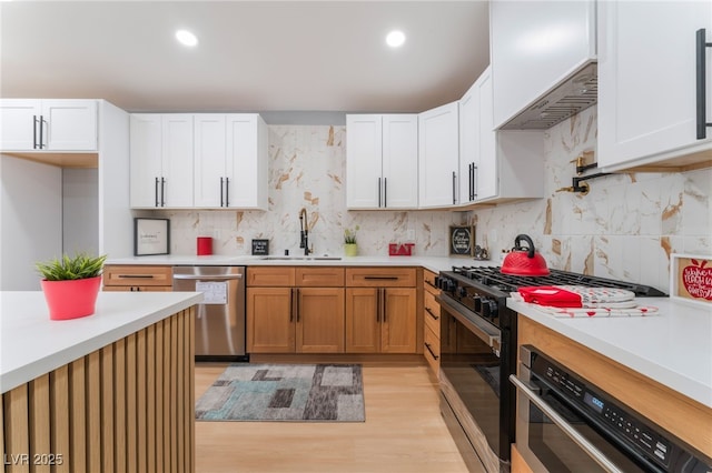 kitchen with stainless steel dishwasher, gas range, a sink, light countertops, and light wood-style floors
