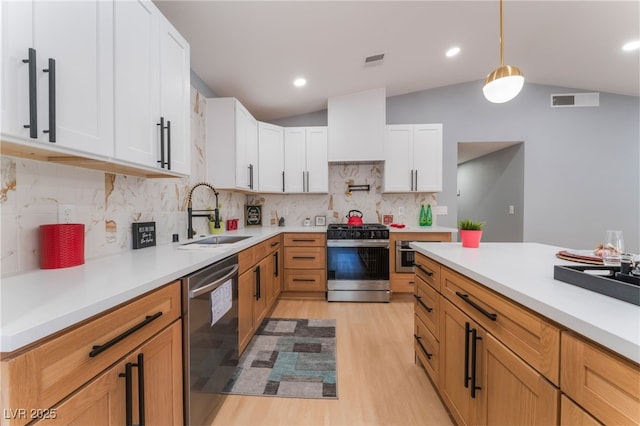 kitchen with stainless steel range with gas stovetop, a sink, dishwashing machine, vaulted ceiling, and light wood-style flooring