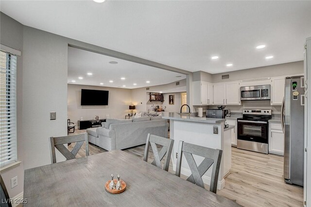 2224 Lucerne Ct, Henderson, NV 89014 - kitchen featuring stainless steel appliances, open floor plan, white cabinets, a peninsula, and light wood-type flooring
