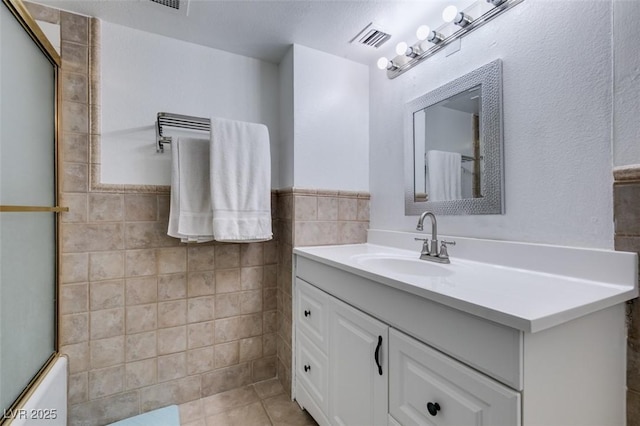 bathroom featuring tile walls, vanity, tile patterned flooring, wainscoting, and a shower