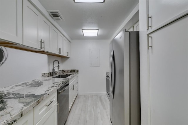 kitchen featuring stainless steel appliances, a sink, light stone counters, light wood-type flooring, and white cabinets