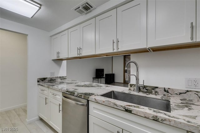 kitchen with stainless steel dishwasher, a sink, white cabinetry, light stone countertops, and baseboards