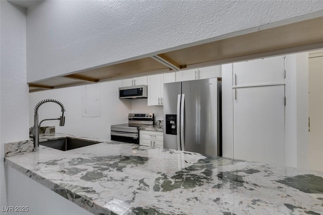 kitchen featuring appliances with stainless steel finishes, a sink, white cabinets, light stone counters, and a peninsula