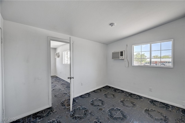 empty room featuring a wall unit AC, lofted ceiling, and baseboards