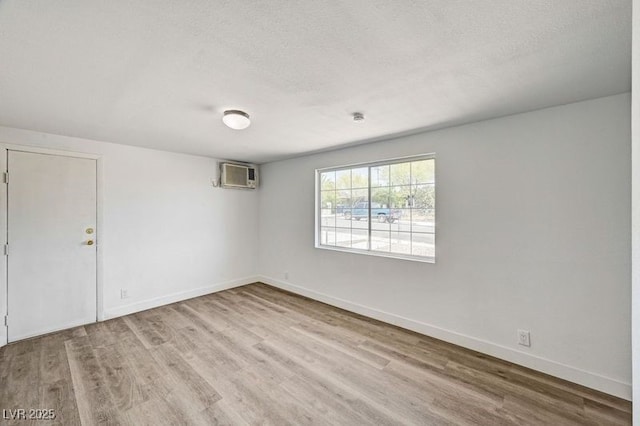spare room featuring wood finished floors, baseboards, a wall mounted air conditioner, and a textured ceiling
