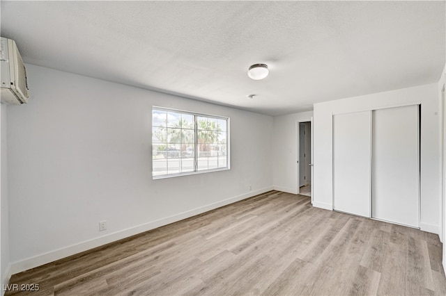 unfurnished bedroom featuring light wood finished floors, a wall mounted air conditioner, a closet, baseboards, and a textured ceiling