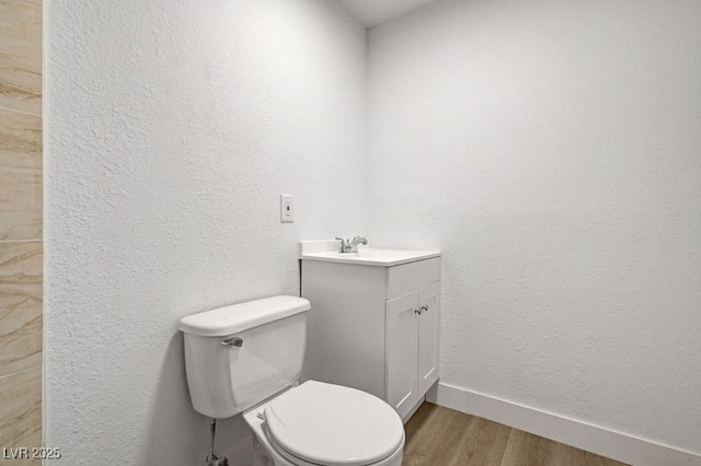 half bathroom with toilet, wood finished floors, vanity, and baseboards