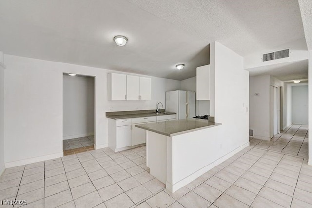 kitchen with freestanding refrigerator, a sink, light tile patterned floors, white cabinetry, and baseboards