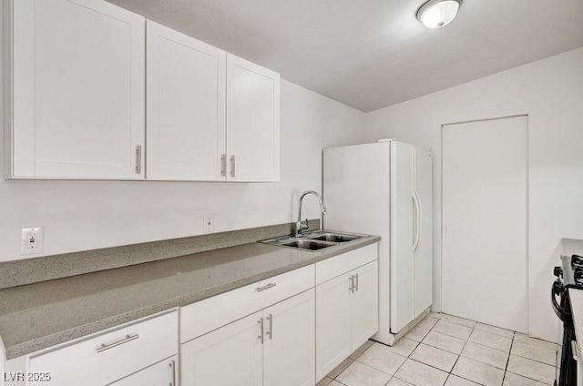 kitchen with a sink, white cabinetry, freestanding refrigerator, light tile patterned floors, and black range oven