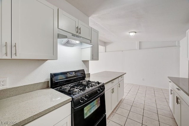 kitchen featuring black range with gas stovetop, under cabinet range hood, white cabinetry, light tile patterned floors, and light stone countertops