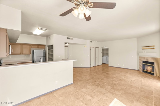 4830 Grey Wolf Ln Unit 104, Las Vegas, NV 89149 - unfurnished living room featuring independent washer and dryer, a ceiling fan, a tiled fireplace, arched walkways, and baseboards