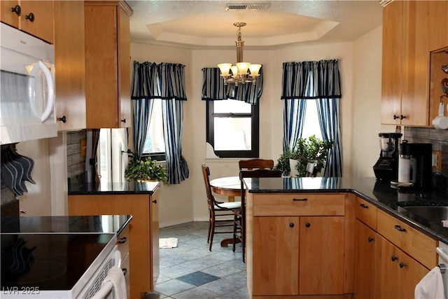 kitchen featuring white microwave, a peninsula, a raised ceiling, tasteful backsplash, and a chandelier