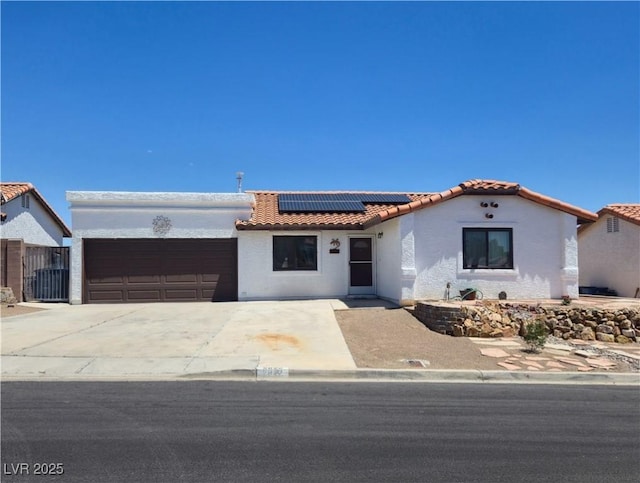 mediterranean / spanish-style home with a tile roof, an attached garage, solar panels, stucco siding, and concrete driveway