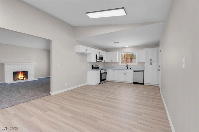 kitchen featuring stainless steel appliances, light wood-style flooring, white cabinets, baseboards, and open floor plan