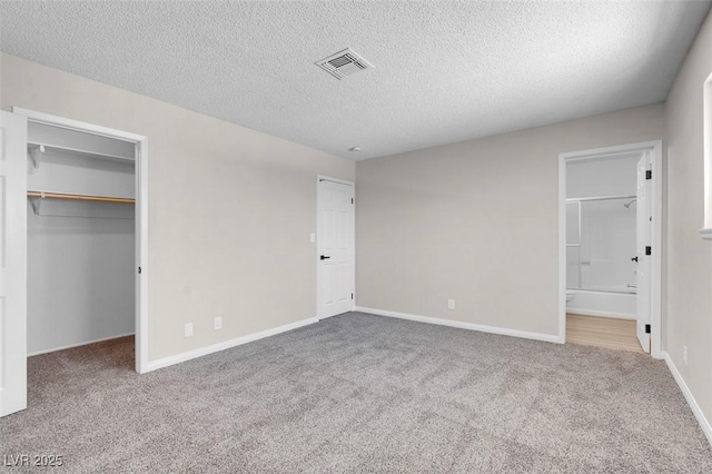unfurnished bedroom with a spacious closet, carpet flooring, a textured ceiling, connected bathroom, and baseboards