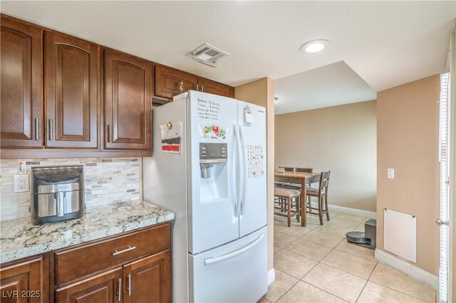 824 Schooner Dr, Henderson, NV 89015 - kitchen featuring white refrigerator with ice dispenser, baseboards, tasteful backsplash, light stone counters, and light tile patterned floors