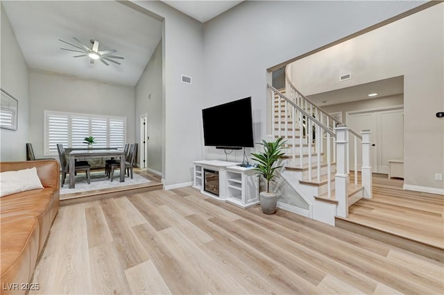 living room with high vaulted ceiling, wood finished floors, baseboards, ceiling fan, and stairway