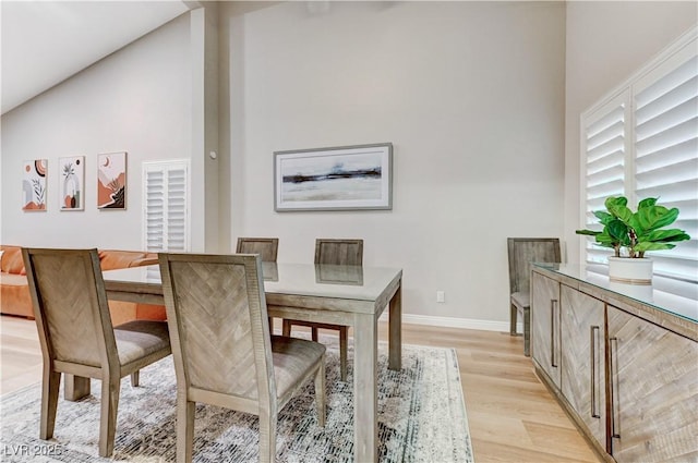 dining area with light wood-style flooring, high vaulted ceiling, and baseboards