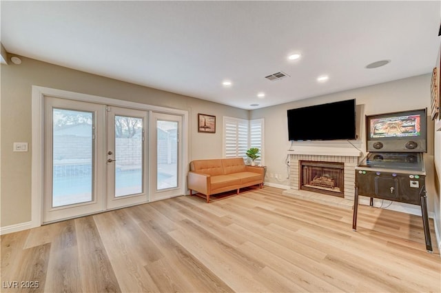 living area with light wood finished floors, french doors, baseboards, recessed lighting, and a brick fireplace