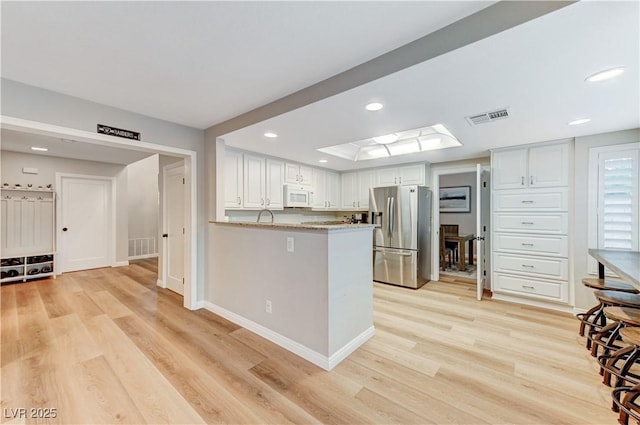 kitchen with stainless steel refrigerator with ice dispenser, white microwave, light wood-style floors, white cabinets, and recessed lighting