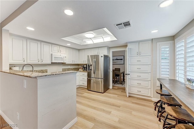 kitchen with stainless steel refrigerator with ice dispenser, white microwave, light stone countertops, light wood-style flooring, and a peninsula