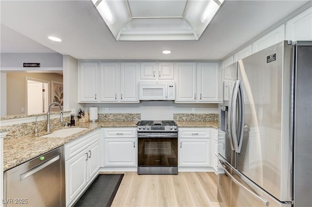 kitchen with stainless steel appliances, a sink, white cabinets, light wood-style flooring, and recessed lighting