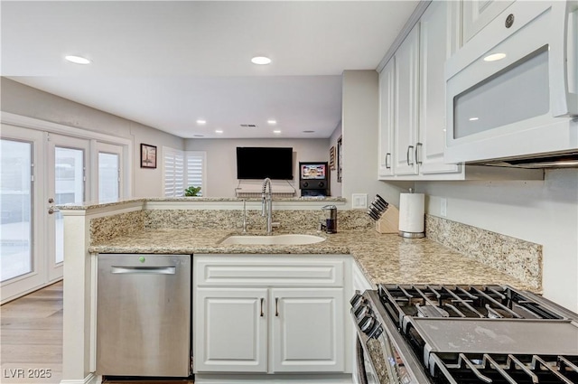 kitchen with appliances with stainless steel finishes, a sink, a peninsula, white cabinets, and recessed lighting