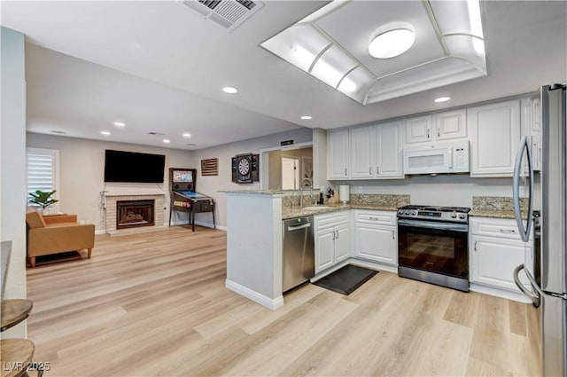 kitchen featuring appliances with stainless steel finishes, open floor plan, white cabinetry, light wood-style floors, and recessed lighting