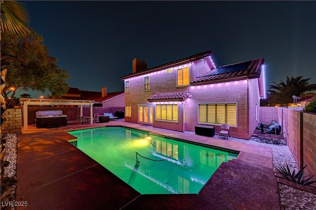 back of house at night featuring a fenced backyard, a jacuzzi, a patio, and a tile roof