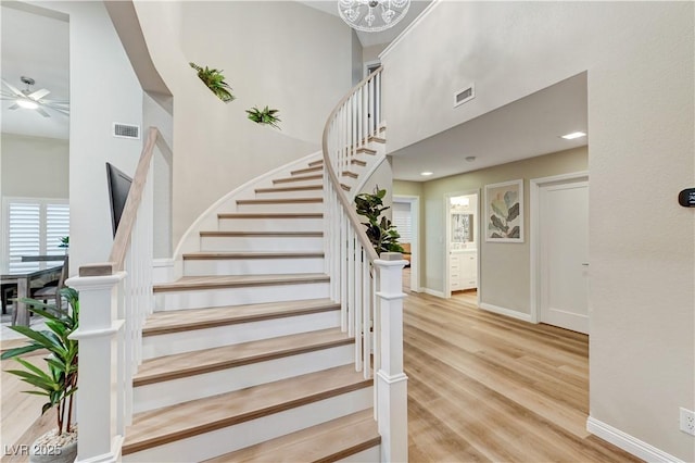 stairs featuring wood finished floors, baseboards, ceiling fan, and a high ceiling