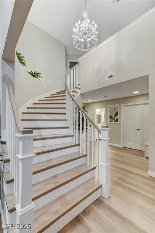 stairs with wood finished floors, a towering ceiling, and a chandelier