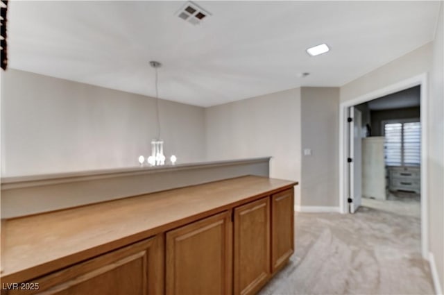 hall with a chandelier, light colored carpet, and baseboards