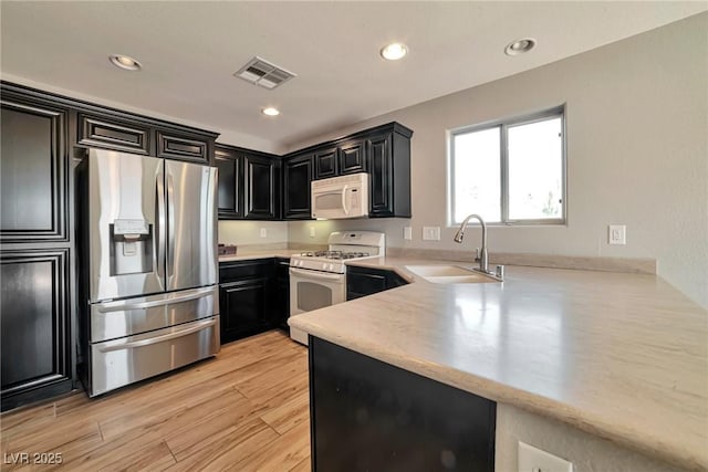 5740 Winter Cherry St, Las Vegas, NV 89130 - kitchen with white appliances, a sink, dark cabinets, light countertops, and light wood-style floors
