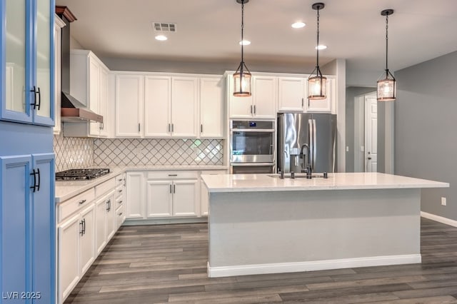 kitchen featuring stainless steel appliances, a sink, backsplash, dark wood-style floors, and a kitchen island with sink