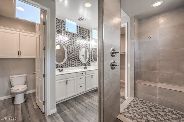 full bathroom featuring wood finished floors, a tile shower, double vanity, toilet, and recessed lighting