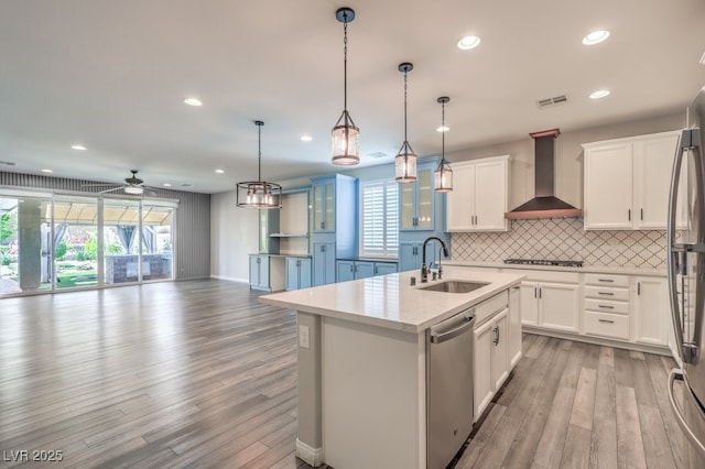 kitchen with a sink, wall chimney exhaust hood, appliances with stainless steel finishes, light wood-style flooring, and healthy amount of natural light