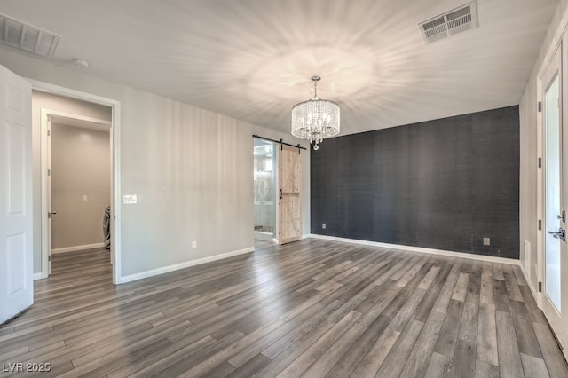 unfurnished dining area with a barn door, a chandelier, wood finished floors, and baseboards