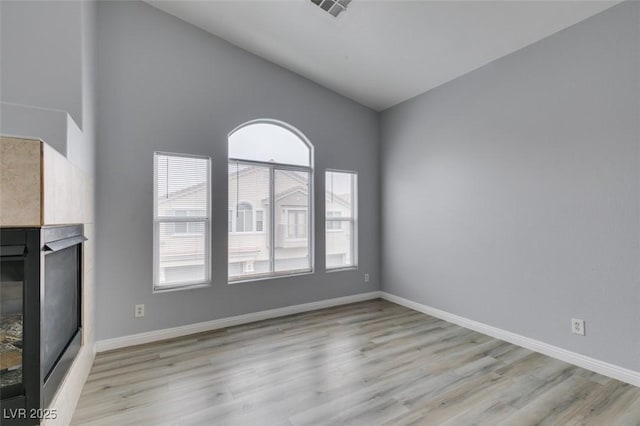 8675 Traveling Breeze Ave Unit 101, Las Vegas, NV 89178 - unfurnished living room with a fireplace, light wood finished floors, baseboards, and lofted ceiling