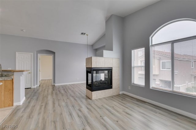 8675 Traveling Breeze Ave Unit 101, Las Vegas, NV 89178 - unfurnished living room featuring arched walkways, light wood-type flooring, a tiled fireplace, baseboards, and high vaulted ceiling