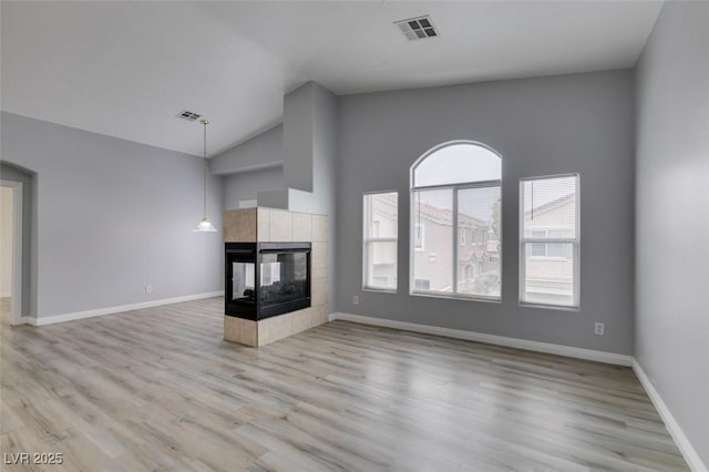 8675 Traveling Breeze Ave Unit 101, Las Vegas, NV 89178 - unfurnished living room with light wood-style flooring, a tiled fireplace, baseboards, and high vaulted ceiling