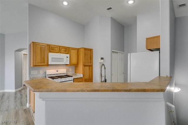 8675 Traveling Breeze Ave Unit 101, Las Vegas, NV 89178 - kitchen with white appliances, a towering ceiling, light wood-style flooring, arched walkways, and a peninsula