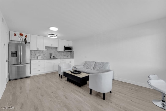 kitchen featuring appliances with stainless steel finishes, light wood-type flooring, a sink, white cabinets, and baseboards