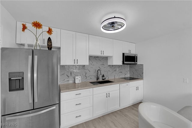 kitchen with stainless steel appliances, a sink, light wood-type flooring, backsplash, and white cabinets