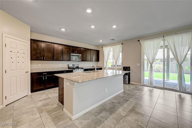 kitchen featuring appliances with stainless steel finishes, a sink, a kitchen island with sink, light stone countertops, and baseboards