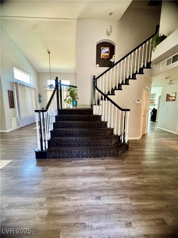 stairway featuring wood finished floors, baseboards, and high vaulted ceiling