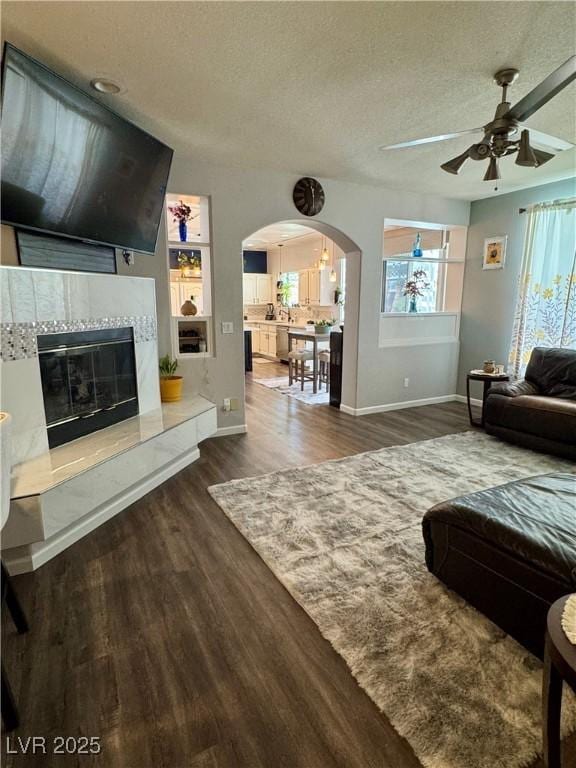 living area with baseboards, ceiling fan, wood finished floors, arched walkways, and a textured ceiling