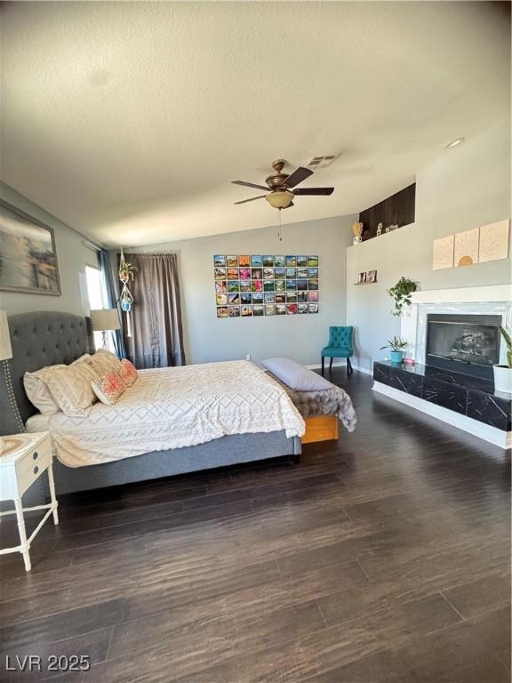 bedroom with a high end fireplace, wood finished floors, and ceiling fan